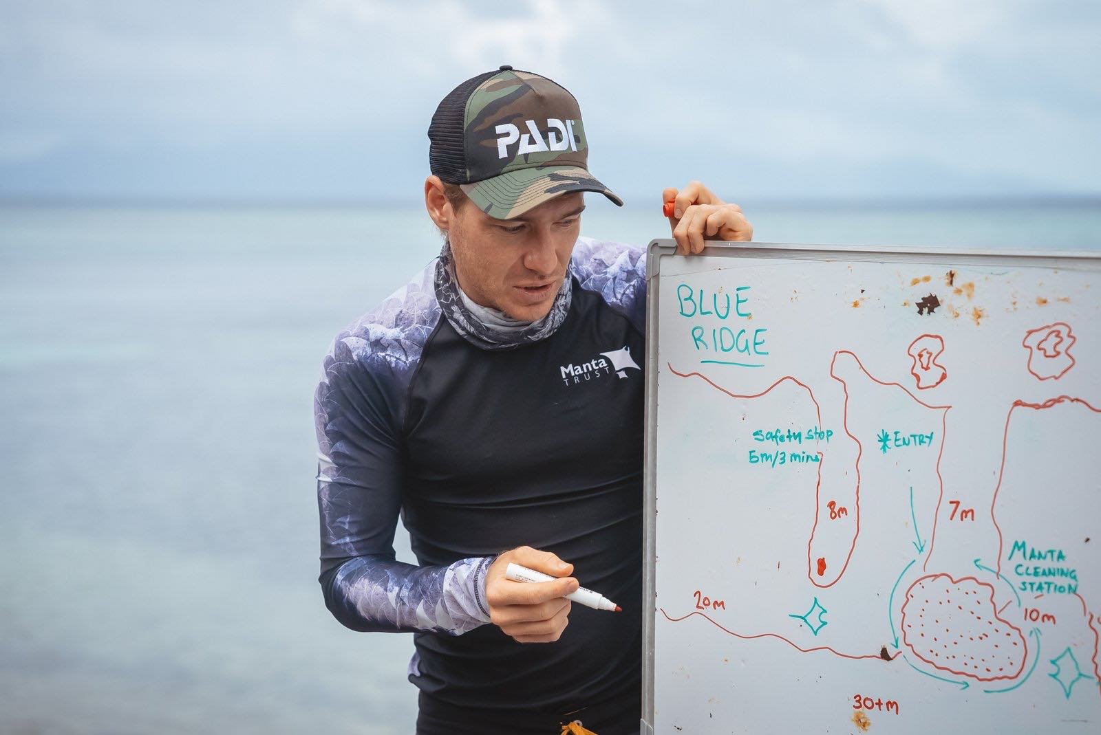 An instructor briefing divers at a whiteboard before a dive