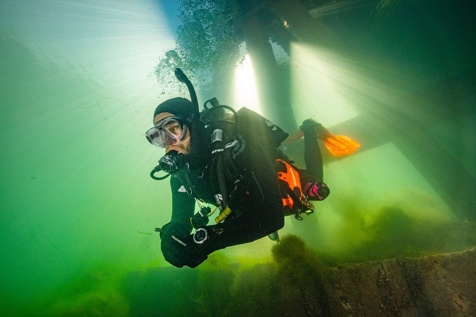 A diver in a drysuit at the water's edge